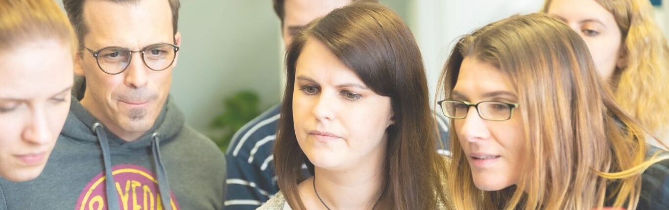 Sechs Teilnehmer schauen in einen Laptop hinein um sich über Comando - Coaching und Managementseminare zu informieren.