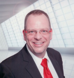 Jens Stührck, gekleidet mit einem dunklblauem Jacket und einer roten Kravatte - Jens Stührck ist der Gründer und Inhaber von Compando - Coaching & Management-Seminare